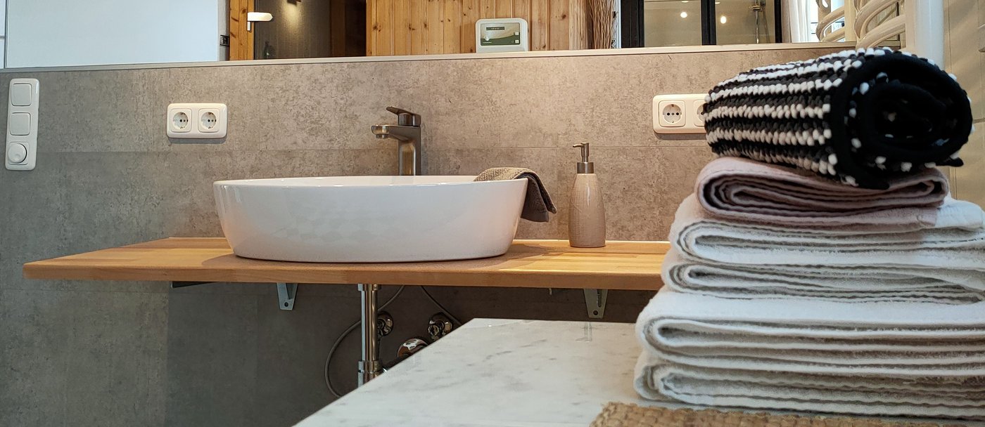 Waschtisch auf Holzplatte mit Spiegel und Handtüchern im ersten Badezimmer der Ferienwohnung Panorama